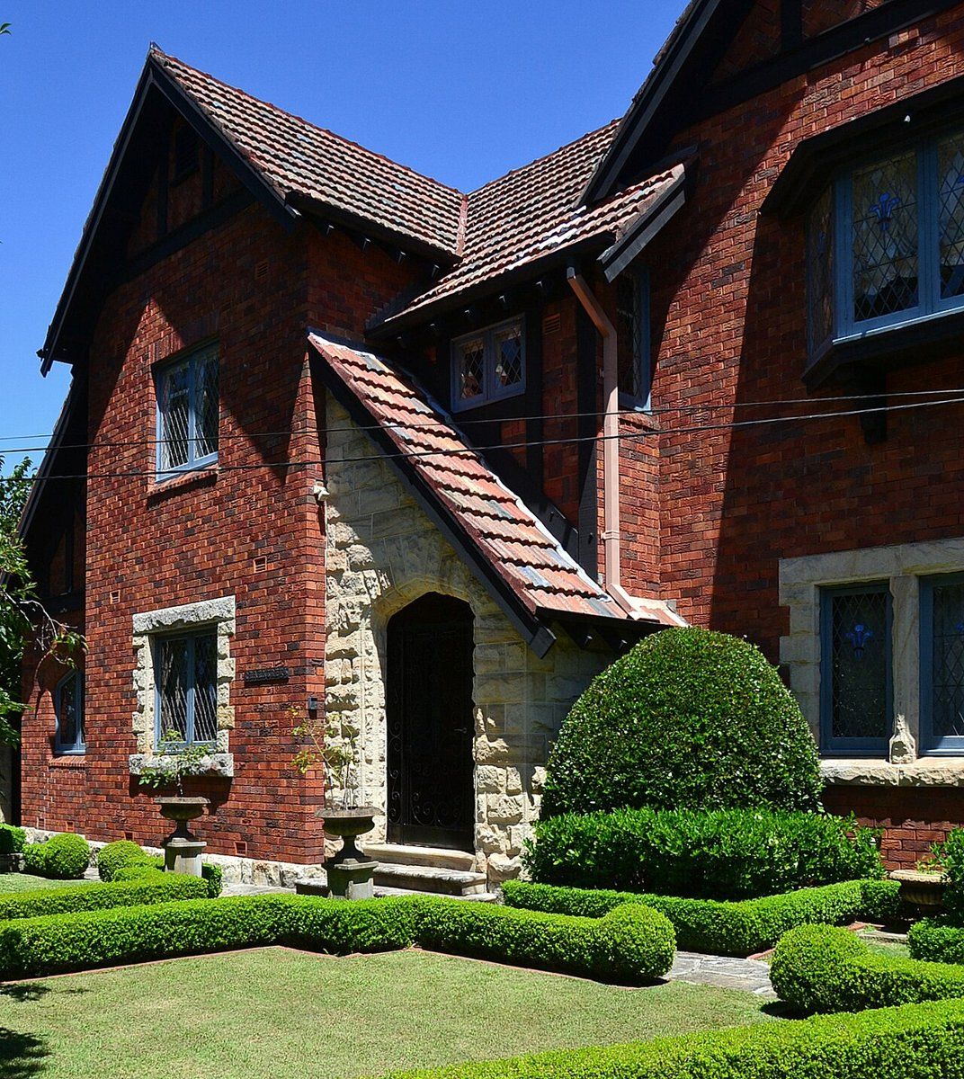 A red-brick house with steep gables and clipped topiary hedges on Heydon Avenue, Warrawee