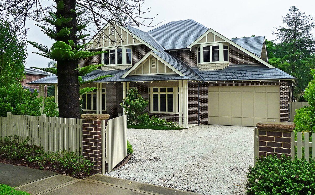 A two-storey house with a gravel driveway, picket fence and a Norfolk Island pine on Middle Harbour Road, East Lindfield